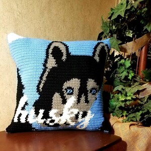 May include: A blue and black crocheted pillow with a husky dog face and the word "Husky" in white lettering.