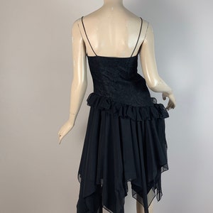 May include: Black sleeveless dress with a lace bodice and a layered, asymmetrical chiffon skirt.