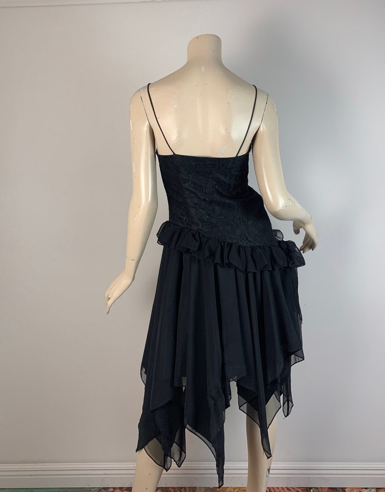 May include: Black sleeveless dress with a lace bodice and a layered, asymmetrical chiffon skirt.