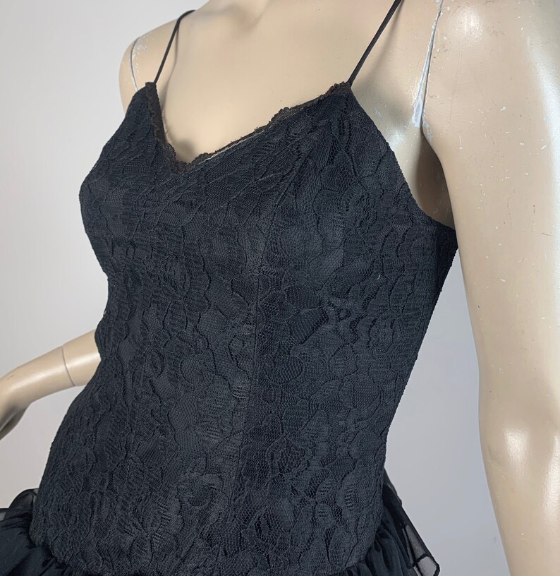 May include: A black lace dress with a ruffled hem. The dress has a V-neckline and spaghetti straps.