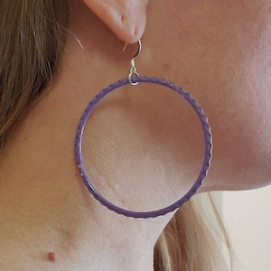 Könnte beinhalten: Ein Paar große, violette Creolen mit einer strukturierten Oberfläche. Die Ohrringe sind aus einem leichten Material gefertigt und haben einen silbernen Haken.