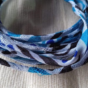 Könnte beinhalten: Ein aufgerolltes Stoffband mit einem sich wiederholenden Muster aus abstrakten Formen in Hellblau, Dunkelblau und Schwarz auf weißem Grund. Das Band weist eine gewebte Textur auf und ist zu einer kreisförmigen Form gewickelt.