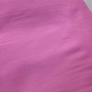 May include: A solid, vibrant magenta fabric with a visible woven texture. The material displays subtle horizontal folds and creases across its surface, showing a consistent, deep pink colour throughout the entire visible area of the textile.