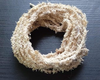 May include: A coiled length of beige, textured yarn with a frayed, fuzzy appearance. The material features a loose, uneven weave with numerous small, protruding fibers throughout the strand, creating a soft and tactile surface texture.