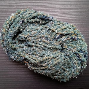 May include: A ball of textured yarn in shades of teal, blue, and brown. The yarn appears to be tightly wound, with a slightly irregular shape. The fibers have a fuzzy, almost frayed appearance, suggesting a handmade or rustic quality. The yarn is likely used for knitting or crocheting.