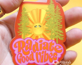 May include: A sticker with a retro sun and trees design. The sticker says "Radiate Good Vibes" in a pink and orange font.