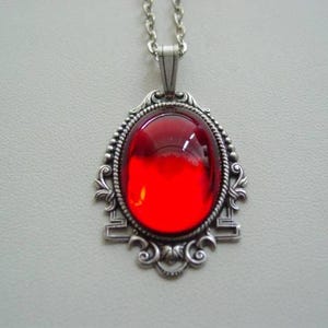 May include: A silver pendant necklace with a large, red, oval-shaped glass stone set in a decorative frame.