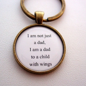 May include: A bronze-colored keychain with a round glass charm that reads "I am not just a dad, I am a dad to a child with wings."