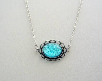 May include: Silver-toned necklace featuring an oval pendant with a vibrant turquoise-colored center. The pendant is framed by a decorative, openwork border. The chain is delicate and simple, creating an elegant accessory.