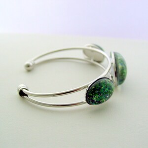 May include: Silver bangle bracelet with three green and blue oval-shaped cabochon stones.