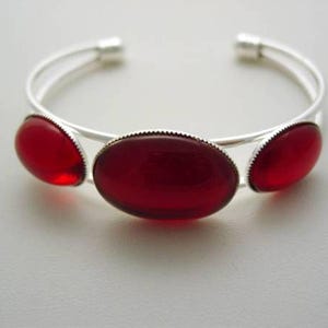 May include: A silver bangle bracelet with three red oval-shaped stones.