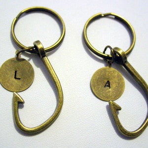 May include: Two gold-toned keychains with a hook shape and a round charm. The charms have the letters "L" and "A" engraved on them.
