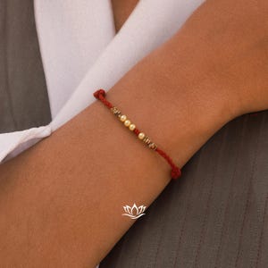May include: A red string bracelet with small gold beads and white pearls.