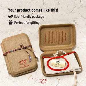 May include: Red string bracelet with a wooden bead that says "How Solace" in a small, brown cardboard box with a red and white string tied around it. The box is on a white surface.