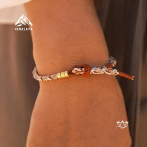 Peut inclure: Un bracelet en cuir tressé avec des perles dorées. Le bracelet est brun, blanc et gris.