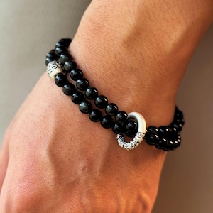 Peut inclure: Un bracelet de perles noires avec des accents argentés. Le bracelet est composé de petites perles noires rondes. Il possède un fermoir argenté avec un motif décoratif.