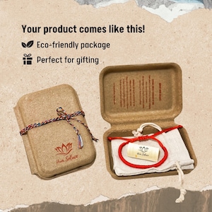 May include: A red cord bracelet with a small cylindrical tag featuring a lotus logo and the text Hum Solace, presented inside a brown molded fiber box with a beige fabric pouch, tied with a multicolored string and branded with a lotus logo.