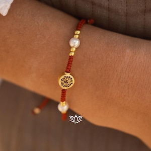 Pode incluir: Um bracelete de corda vermelha com um fecho de filigrana dourada e contas de pérola branca.