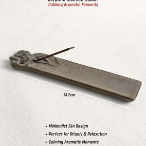 May include: A ceramic incense holder, 14.2cm long, with a minimalist Zen design. The holder is a muted gray color and features the text "Ceramic Incense Holder Calming Aromatic Moments". An incense stick is placed in the holder.