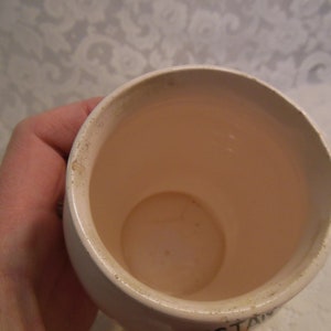 Peut inclure: Une tasse en c&eacute;ramique blanche avec un int&eacute;rieur rose clair. Le bord de la tasse pr&eacute;sente une d&eacute;coloration. La tasse est tenue par une personne.