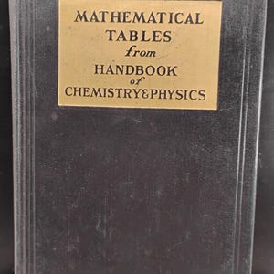 May include: A vintage book titled "MATHEMATICAL TABLES from HANDBOOK of CHEMISTRY&PHYSICS." The cover is dark with a gold rectangular label. The book's title is in bold, black font. The book is a reference guide for chemistry and physics.