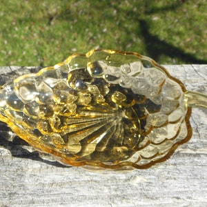 May include: A small, amber-colored glass dish shaped like a bunch of grapes. The dish has a scalloped edge and a textured surface.