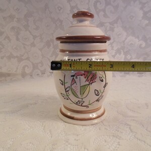 Peut inclure: Pot &agrave; caf&eacute; instantan&eacute; en c&eacute;ramique, d'environ 13 cm de haut, avec couvercle. Le pot est blanc cass&eacute; avec des accents bruns et un motif peint &agrave; la main d'oiseau et de fleurs. Le texte "INSTANT COFFEE" est imprim&eacute;.