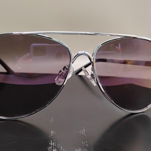 May include: Aviator sunglasses featuring a thin, polished silver metal frame with a double bridge design. The lenses are gradient-tinted, transitioning from a darker shade at the top to a lighter, translucent tone toward the bottom, with clear nose pads.