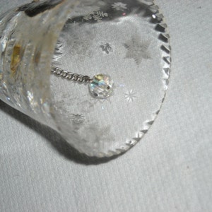 K&ouml;nnte beinhalten: Eine klare Glasglocke mit einem Kristall, der an einer Kette im Inneren h&auml;ngt. Die Glocke hat ein dekoratives, ge&auml;tztes Muster aus Schneeflocken.