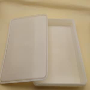 May include: A white rectangular plastic container with a matching lid, slightly ajar. The container and lid are made of a smooth, opaque material. The container is empty.