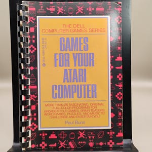 May include: A vintage book titled "Games for Your Atari Computer" by Paul Bunn. The cover is yellow with purple text and a red border. The book is part of "The Dell Computer Games Series."