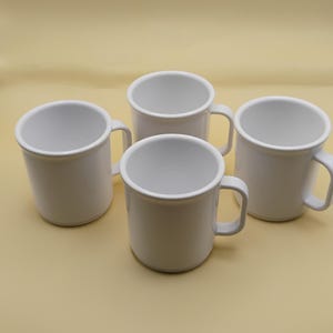 May include: Four white ceramic mugs with handles are arranged on a light yellow surface. The mugs are cylindrical with a slightly flared top and a simple, rounded handle. The mugs are empty.