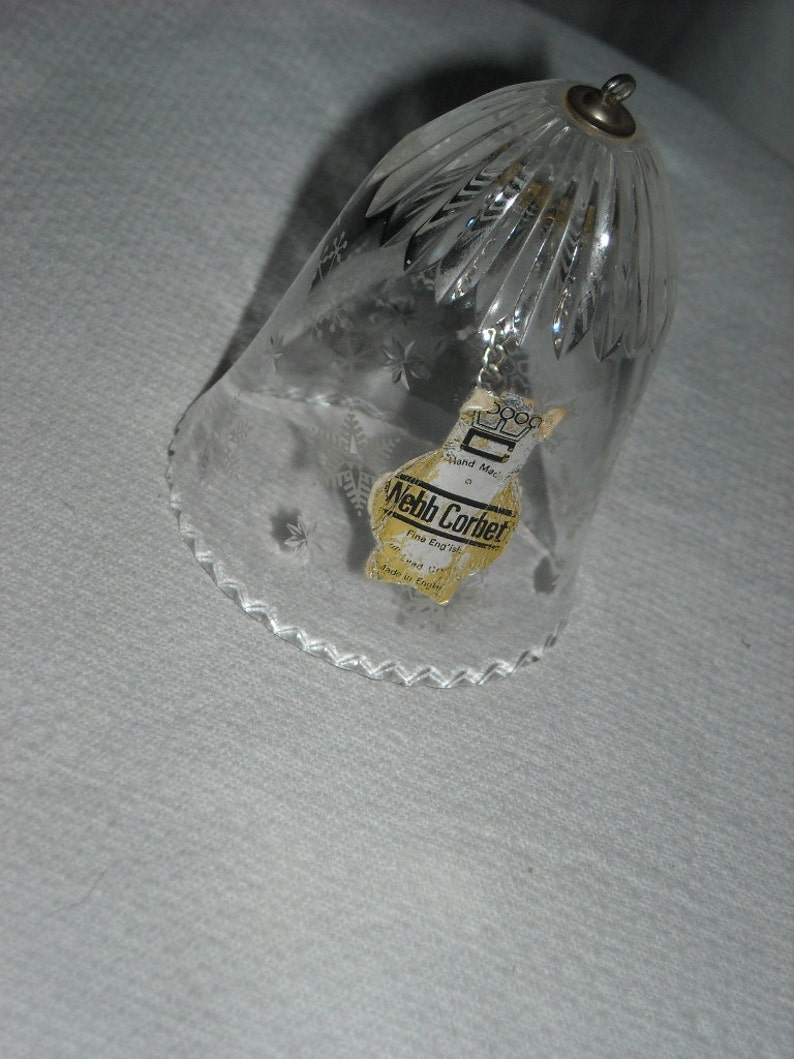 K&ouml;nnte beinhalten: Eine klare Glasglocke mit einem gewellten Rand und einem Schneeflockenmuster. Die Glocke tr&auml;gt ein Etikett mit der Aufschrift "Webb Corbett, Hand Made, Fine English Crystal, Made in England".