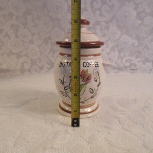 Peut inclure: Pot &agrave; caf&eacute; instantan&eacute; en c&eacute;ramique cr&egrave;me, avec couvercle et base marron. Il mesure environ 13 cm de haut. Il pr&eacute;sente des motifs floraux et de feuilles et les mots "INSTA COFFEE" en noir.