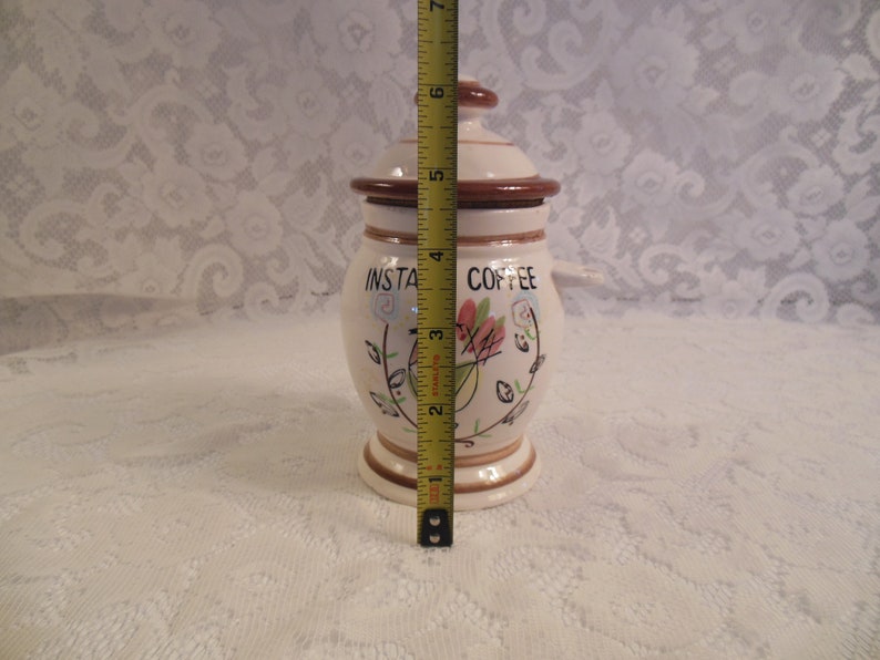 Peut inclure: Pot &agrave; caf&eacute; instantan&eacute; en c&eacute;ramique cr&egrave;me, avec couvercle et base marron. Il mesure environ 13 cm de haut. Il pr&eacute;sente des motifs floraux et de feuilles et les mots "INSTA COFFEE" en noir.