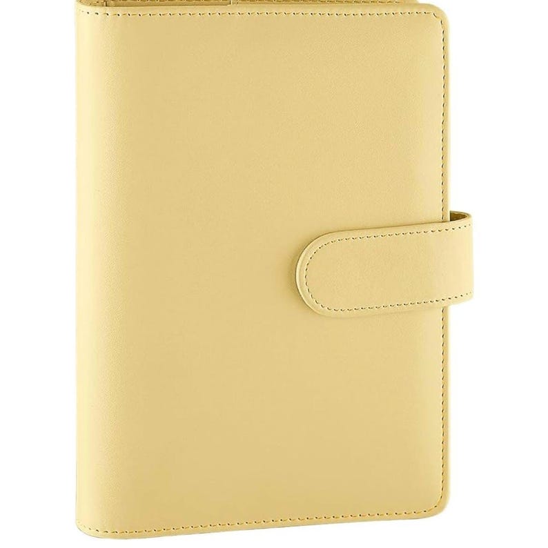 May include: A pale yellow leather bound journal with a flap closure. The journal has a stitched edge and a smooth, matte finish.