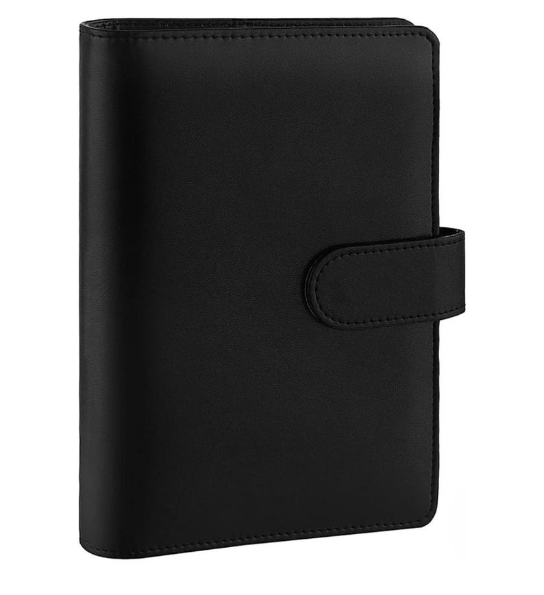 May include: A black leather planner with a flap closure and a strap. The planner has a smooth, textured surface.