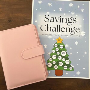 Könnte beinhalten: Ein hellrosa Planer neben einem blau-weißen "Savings Challenge" Blatt. Das Blatt zeigt ein Weihnachtsbaum-Design mit Beträgen von 15€ bis 60€. Der Text lautet "Savings Challenge for Holidays and Special Occasions."