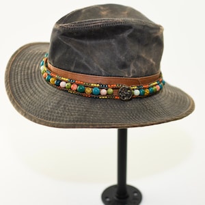 May include: A brown canvas hat with a wide brim and a beaded band. The band is made of leather and has colorful beads, including turquoise, orange, and pink.