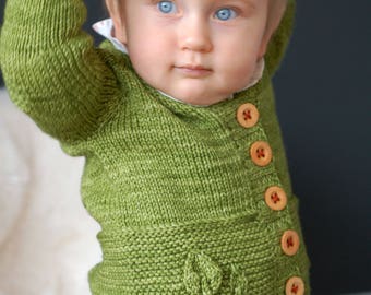 May include: A green knitted cardigan with wooden buttons for a baby or toddler. The cardigan has a leaf design on the front.