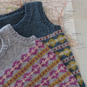 May include: Two knitted vests with geometric patterns. The top vest is blue with yellow, white, and red accents. The bottom vest is gray with pink, yellow, and white accents.