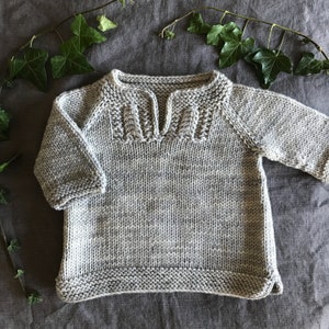 May include: A gray knitted sweater with a V-neck and a detailed knit pattern around the neckline.