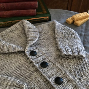 Peut inclure: Un cardigan gris en tricot avec un col châle et trois boutons noirs. Le cardigan est fait d'un fil doux et texturé.