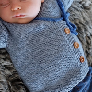 May include: A light blue knitted baby cardigan with brown buttons and a blue tie closure.