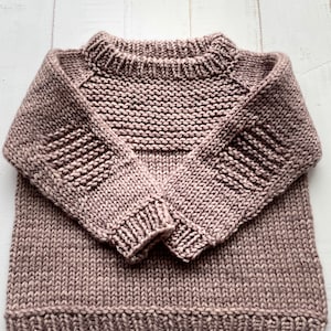 May include: A brown knitted jumper with a crew neck and long sleeves. The jumper has a ribbed texture and a slightly loose fit.