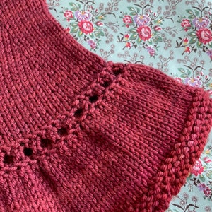 May include: Close-up of a deep red knitted fabric with a decorative stitch pattern along the edge.