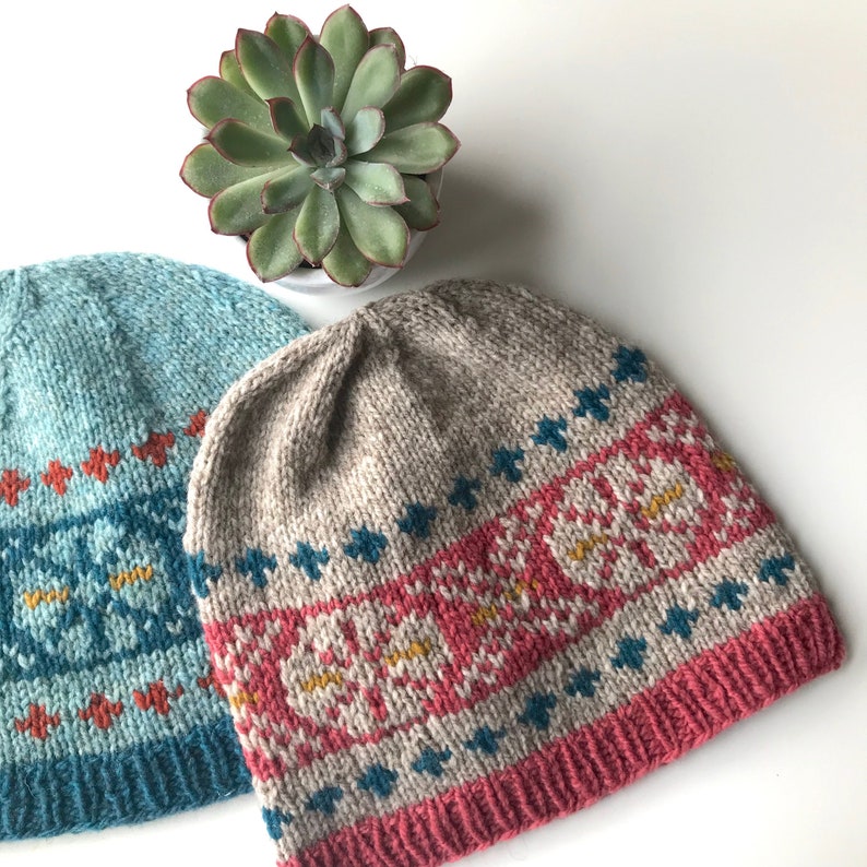 May include: Two knitted hats with colourful geometric patterns. The hat on the left is teal blue with orange and white accents. The hat on the right is beige with pink, orange, and teal blue accents.
