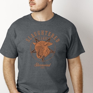 May include: Dark gray t-shirt featuring a distressed orange graphic. The graphic includes the words "Slaughtered Lamb" above a lamb's head within a star, with "Stormwind" and "2001" below. The shirt has a crew neck.