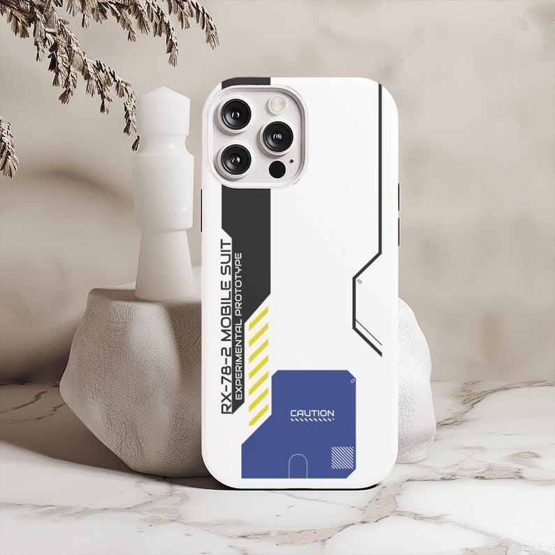 May include: White phone case with a black and gray design. The case has a blue and yellow caution sign with the text "RX-78-2 MOBILE SUIT EXPERIMENTAL PROTOTYPE" and "CAUTION".