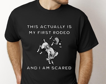 May include: Black t-shirt with a white graphic of a bucking bronco and a rider. The text on the shirt reads "THIS ACTUALLY IS MY FIRST RODEO AND I AM SCARED."